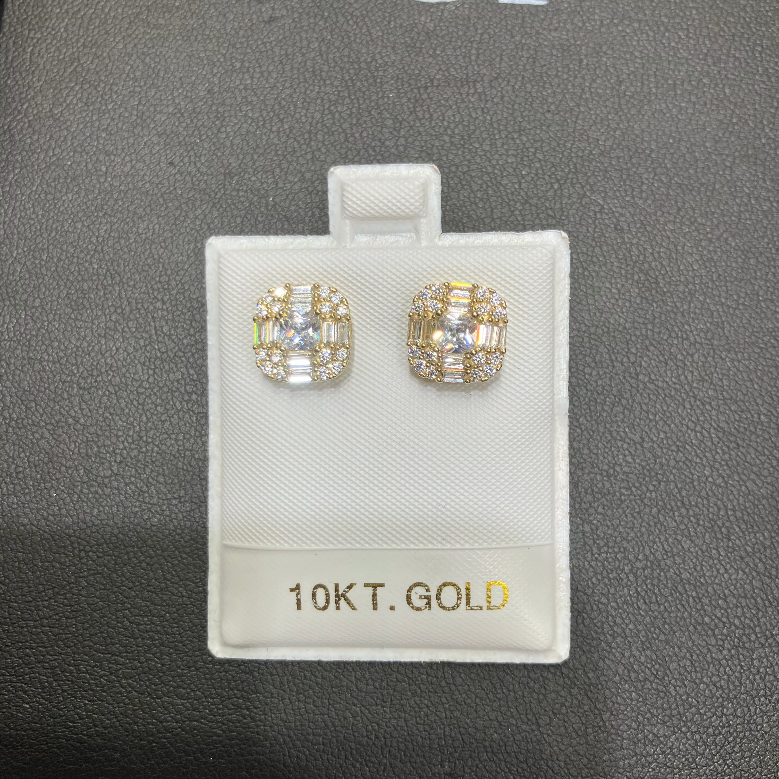 Gold earrings on a display card with '10K T. Gold' text against a dark background.