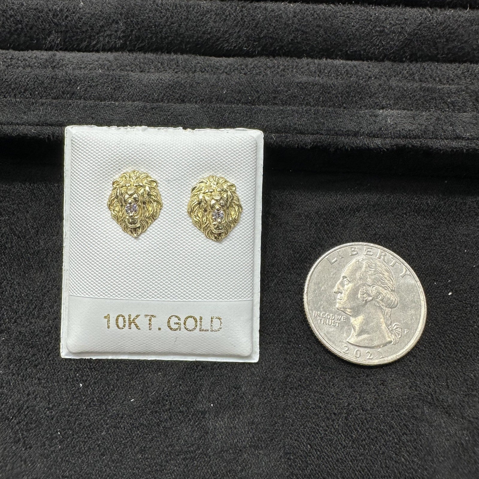 Gold lion head earrings on a display card with a quarter for scale, all on a black background.