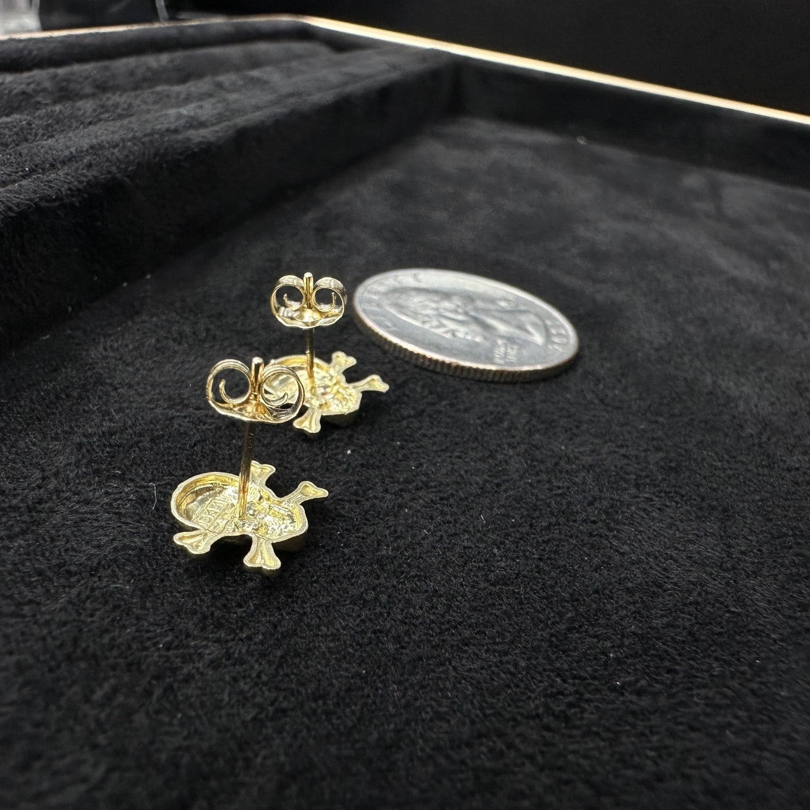 Gold animal-shaped earrings on a black surface with a coin for scale.