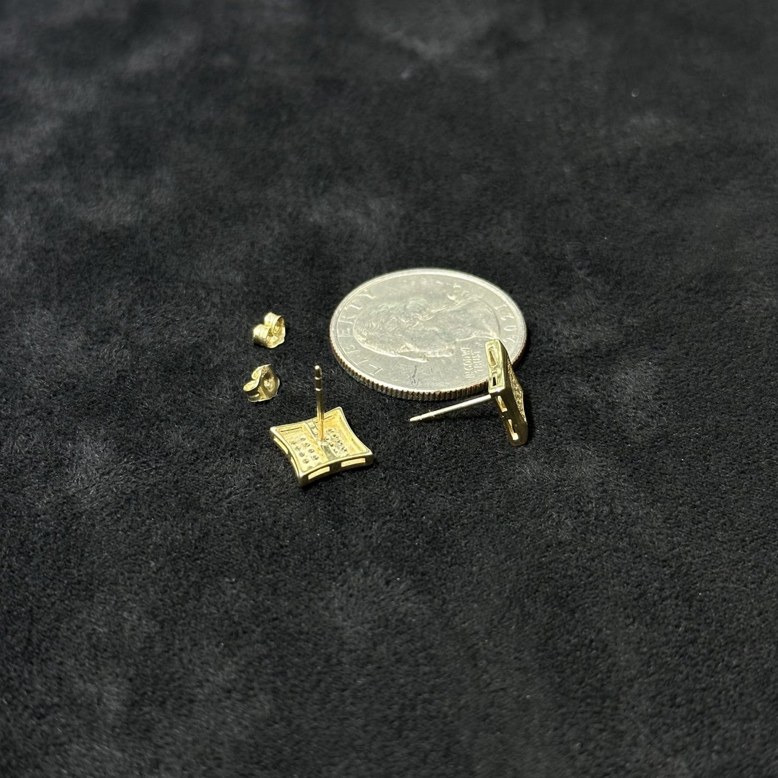 Gold earring components on a black background with a coin for scale.