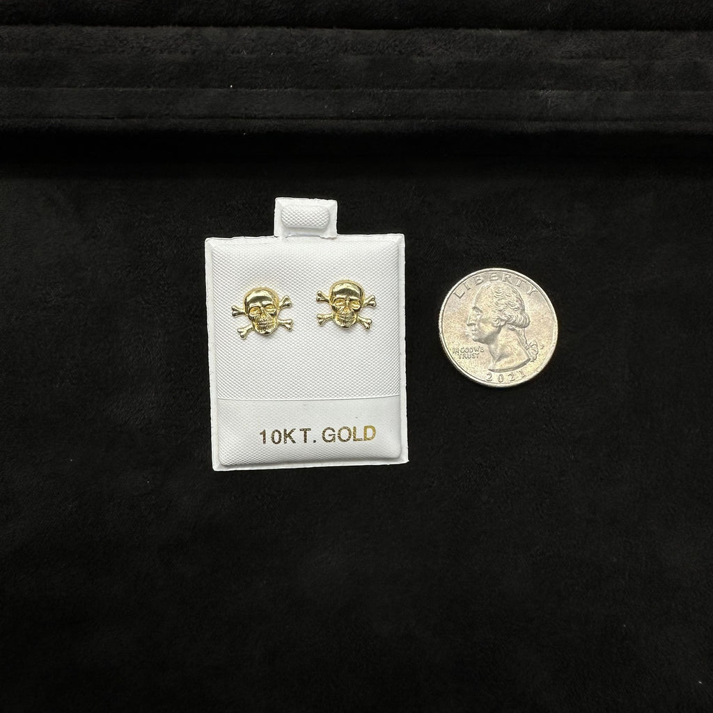 Gold skull earrings on a white card with '10Kt. Gold' text, next to a U.S. quarter coin on a black background.